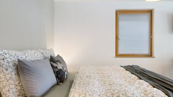 Ein Schlafzimmer mit einem Bett, einem Fenster mit Jalousien und einer Couch mit gemusterten Kissen.