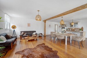 Un grand espace de vie comprenant un canapé, une table basse, une table à manger et des chaises. On aperçoit une cuisine au fond.