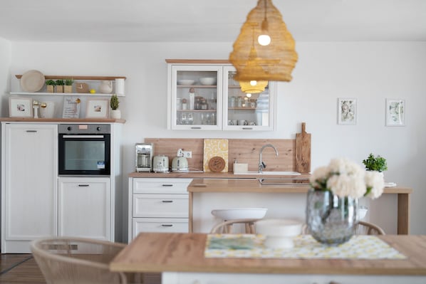 Une cuisine moderne avec des meubles blancs, un plan de travail en bois et un luminaire suspendu.