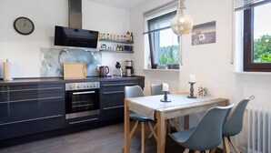 Een moderne keuken met een ingebouwde oven, een koffiezetapparaat en een eethoek met een tafel en stoelen.