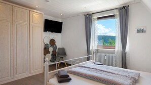 Een slaapkamer met een bed, een televisie, een raam met gordijnen, een stoel en een kledingkast.