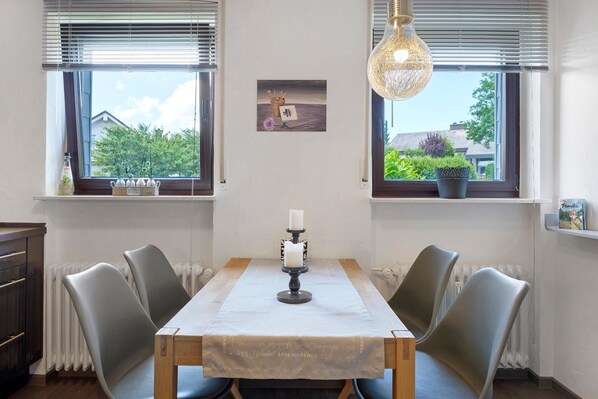 Un coin repas comprenant une table, des chaises, un chandelier et une vue par les fenêtres.
