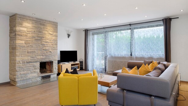 Een moderne woonkamer met een stenen haard, een flatscreen televisie, een bank en een groot raam.