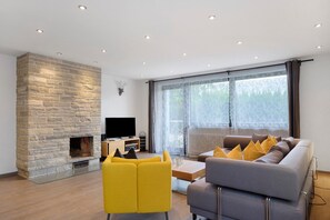 A modern living room with a stone fireplace, a flat-screen TV, a sofa, and a large window. - Holiday Home 'Obergfell, 110 Qm' with Private Terrace, Private Garden and Wi-Fi (Schönwald im Schwarzwald)
