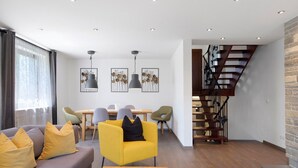 Een moderne woonkamer met een bank, fauteuil, eettafel en trap.