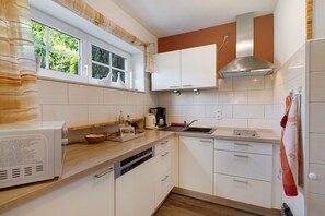 A kitchen with white cabinets, a stainless steel range hood, a window with curtains, and a dishwasher.