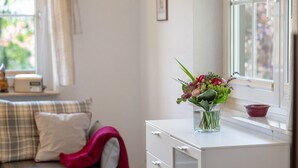 A room with a white desk, a window with a view, a sofa with a plaid cushion, and a vase with flowers on the desk. - Apartment 'Waltraud' with Shared Terrace, Shared Garden and Wi-Fi (Meßstetten)