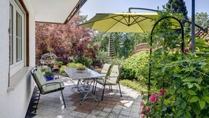 A patio with a table and chairs, a yellow umbrella, and a garden with various plants and flowers. - Apartment 'Waltraud' with Shared Terrace, Shared Garden and Wi-Fi (Meßstetten)