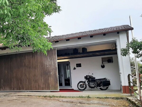 Un edificio moderno con una puerta de garaje, una motocicleta estacionada en el interior y un árbol en primer plano.