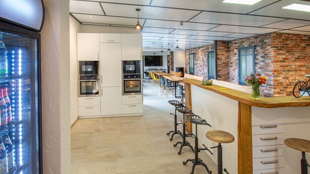 Una cocina moderna con armarios blancos, electrodomésticos de acero inoxidable y una barra alargada con taburetes.