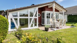 Une maison dotée d’une grande baie vitrée, d’un patio avec une table et des chaises, et d’un jardin bien entretenu.