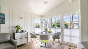 Un coin repas avec une table ronde, quatre chaises, une plante en pot et une vue dégagée grâce à de grandes fenêtres.