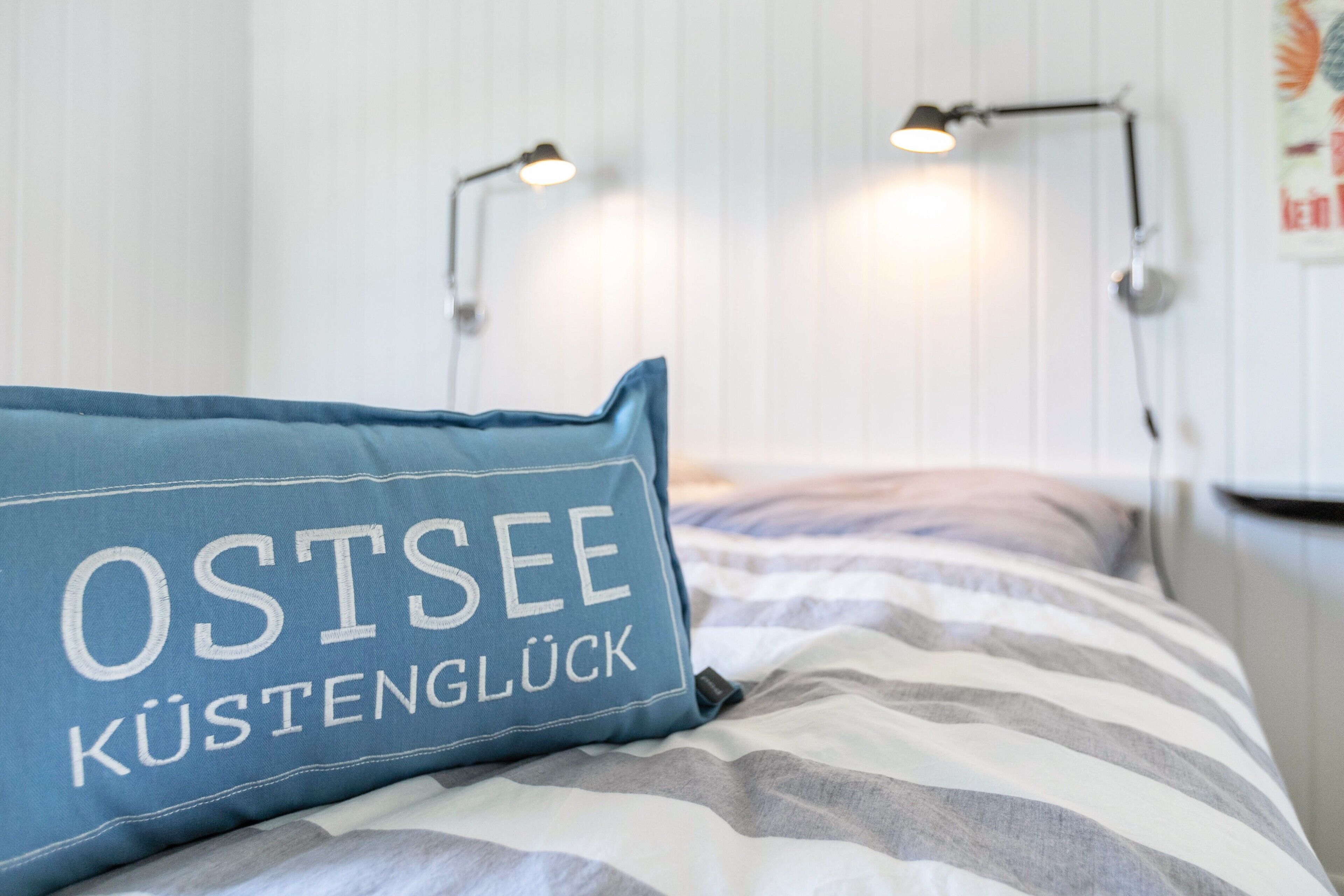 A bed with a striped blanket, a blue pillow with text, and two bedside lamps.