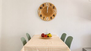 A dining table with a clock, chairs, and a fruit bowl.