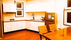 Une cuisine de taille réduite avec des meubles blancs, une table à manger en bois et un réfrigérateur.