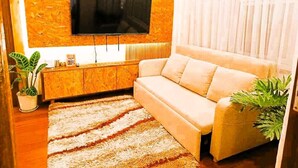 Un salon avec un téléviseur à écran plat fixé à un mur texturé, un canapé beige, un meuble en bois et un tapis à rayures.