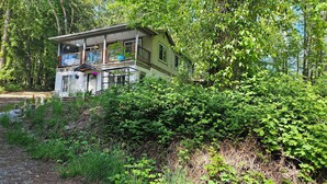 Une maison entourée d’une végétation luxuriante, dotée d’un porche bien visible et d’un petit jardin.