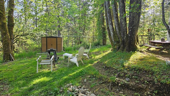 A rustic outdoor setting with a wooden shed, picnic table, and metal chairs.