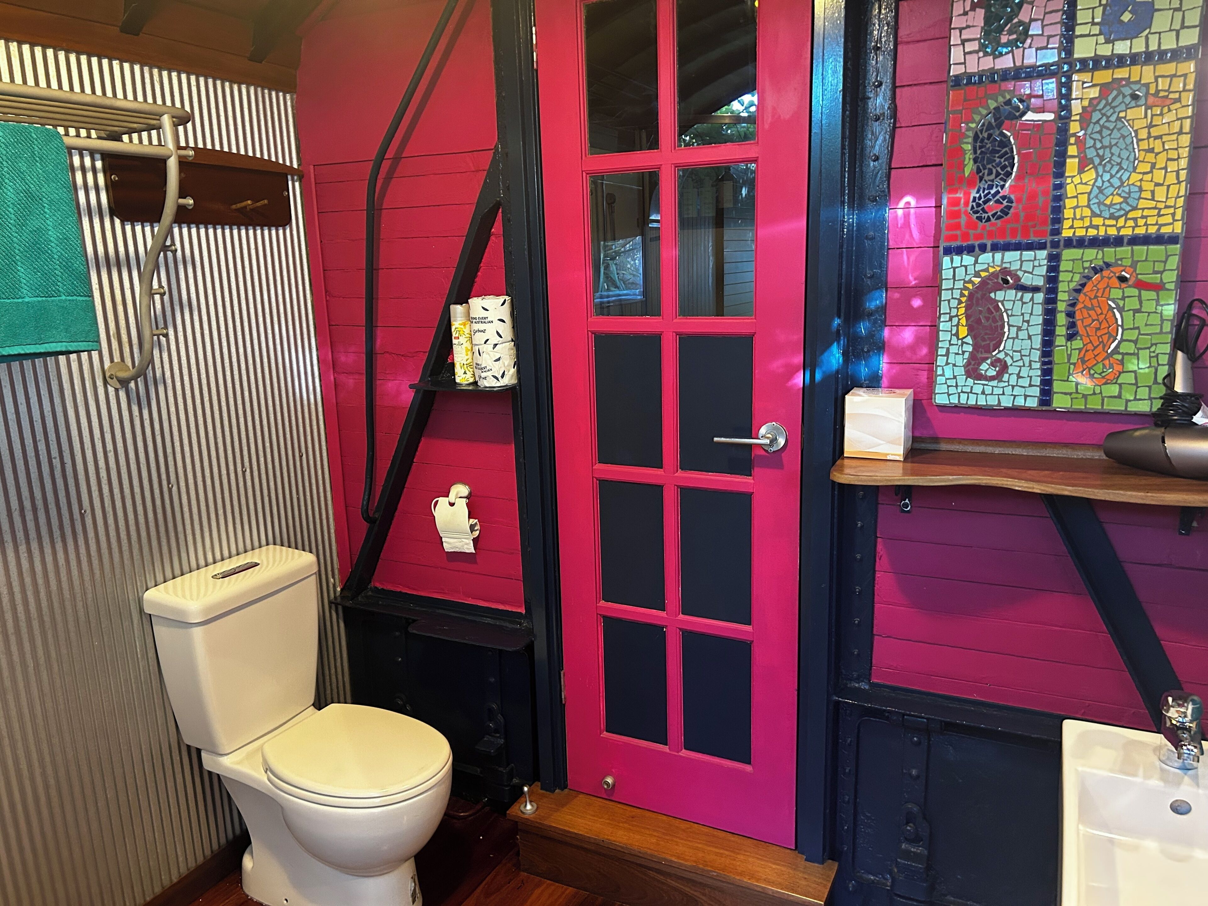 Ein Badezimmer mit Toilette in Weiß, einer rosafarbenen Tür und einer Wand aus Mosaik.