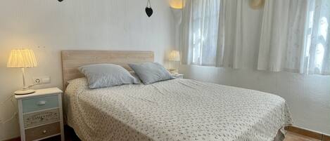 Een net opgemaakt bed met een bloemenbedekking, twee kussens, een bedlampje en een nachtkastje met een lade.