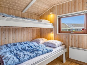 Een slaapkamer met stapelbedden, houten wanden, een raam met uitzicht op een huis en een witte radiator.
