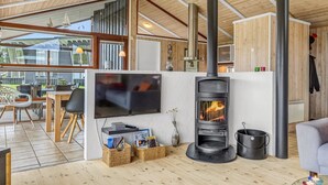Una sala de estar moderna con un televisor grande, una estufa de leña y un comedor con vistas al exterior.