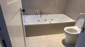 Kylpyhuone, jossa on kylpyamme, wc ja laatoitettu lattia.