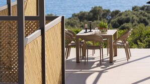 An outdoor patio with a table and chairs, overlooking a scenic view of the sea and hills.