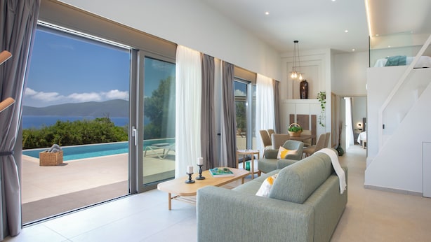 A modern living room with a large sliding glass door leading to a pool area, a sofa, a coffee table, and a dining area with chairs. - Villa Virgo Ammoussa Lefkada (Lefkada)