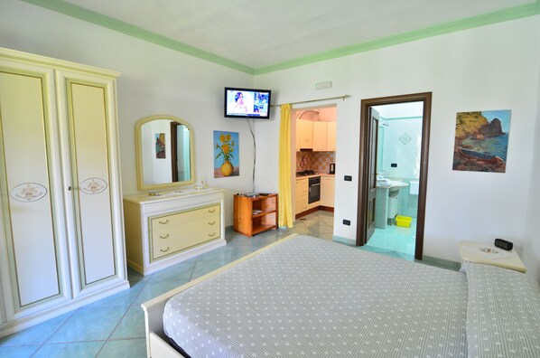 Une chambre à coucher comprenant un lit, une commode, un téléviseur et une salle de bain visible à travers une porte ouverte.