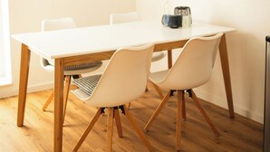 Un comedor con una mesa blanca, sillas de madera y un televisor de pantalla plana montado en la pared.