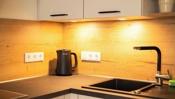 Una cocina moderna con armarios blancos, encimera negra, horno empotrado, cafetera y lavabo con grifo.