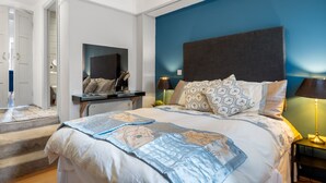 A bedroom with a large bed, a bedside table, a nightstand, a mirror, and a view of the bathroom.