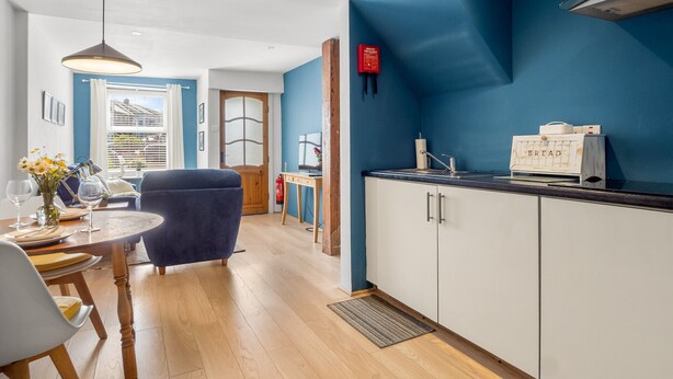 A modern kitchen with white cabinets, a blue accent wall, a wooden dining table, and a blue chair.