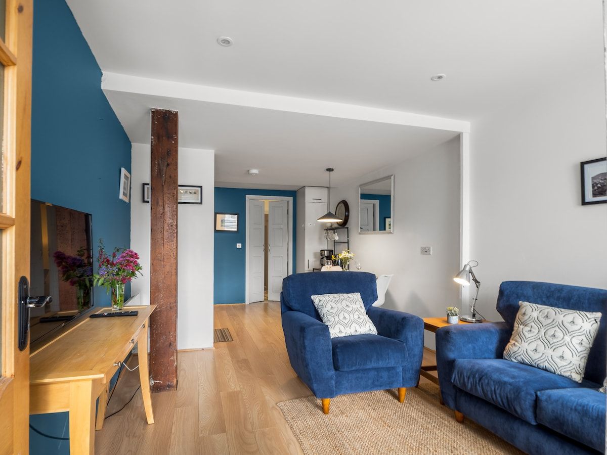 A modern living room with a blue sofa, a wooden coffee table, and a kitchen area in the background.