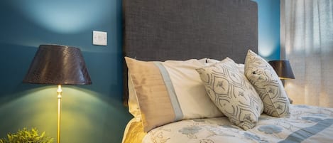 A neatly made bed with floral bedding, a bedside lamp, and a clock on a bedside table.