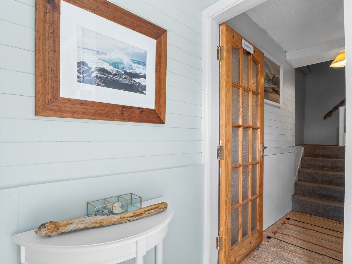 A hallway with a wooden door, a framed picture on the wall, and a small white table with decorative items.