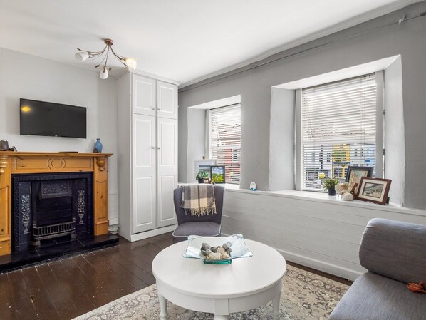 A living room with a fireplace, a television, a round coffee table, and a window with blinds.