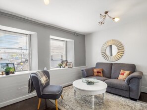 A living room with a grey sofa, a round mirror, and a white coffee table. - Clifden Nook 2 Apt w/ Fireplace (Clifden)