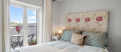 A bedroom with a bed, a nightstand, a lamp, and a view of the outside.