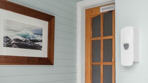A room with a wooden door labeled "Apartment 2," a framed picture of a seascape, and a white wall-mounted soap dispenser. - Clifden Nook 2 (Clifden)