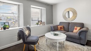 A living room with a grey sofa, a round coffee table, and a decorative mirror on the wall. - Clifden Nook 2 (Clifden)