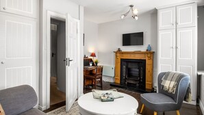 A living room with a fireplace, a television mounted above it, and a round white coffee table. - Clifden Nook 2 (Clifden)