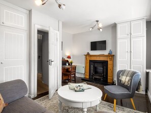 A living room with a fireplace, a television mounted above it, and a round coffee table with decorative items. - Clifden Nook 2 Apt w/ Fireplace (Clifden)