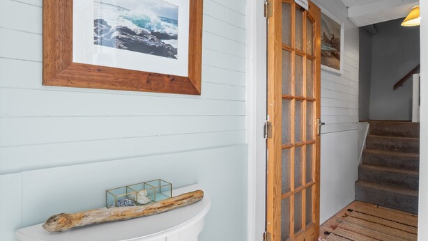A hallway with a wooden door labeled "Apartment 2," a framed photograph on the wall, and a small table with a decorative object. - Clifden Nook 2 (Clifden)