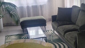 Un salón con sofá, un sillón verde, una mesita de centro y una planta grande en maceta.