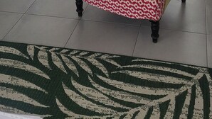 Una sala de estar con un sillón estampado, un comedor con mesa y sillas de madera, un refrigerador negro y un reloj en la pared.