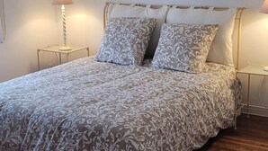 Una cama bien hecha con una colcha estampada y dos almohadas, una lámpara de noche y una mesita con una lámpara encima.