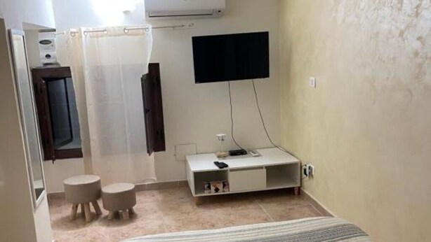 Une chambre d’hôtel avec un lit, un téléviseur fixé au mur, une petite armoire blanche et un espace douche séparé par un rideau.