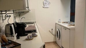 Une cuisine compacte équipée d’un grille-pain, d’un lave-linge et d’un petit plan de travail sur lequel se trouvent une horloge et une tasse.